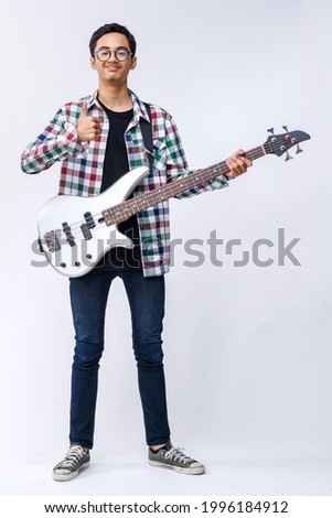 Full-body portrait shot of handsome young teenage musician holding a bass guitar in studio. Professional young junior bassist smiling and looking at camera isolated with white background