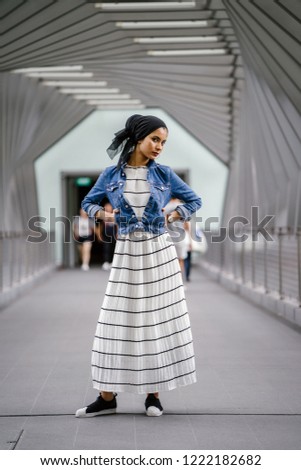 A full-body portrait of a tall, elegant and slim young Middle Eastern woman standing in the walkway of a beautiful bridge (geometric patterns).  She has her arms on her hips and is making a funny face