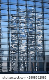 Full-frame abstract view of a modern blue glass skyscraper facade with dramatic wavy reflections of neighboring high-rises.