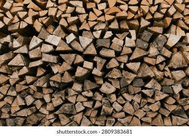 Full-frame background texture of split firewood logs. A close-up, full-frame texture of chopped and stacked firewood logs showing varying shades of wood and bark. Natural rustic background and pattern material.