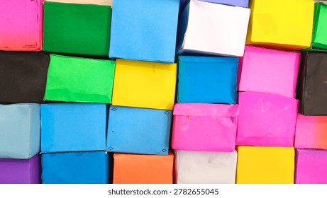 A full-frame background texture of various small handmade paper gift boxes in vibrant colors like pink, blue, yellow, and green, neatly stacked together side by side.