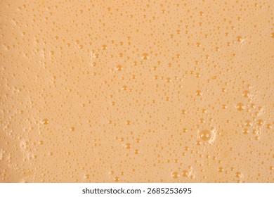 A full-frame, close-up shot captures the texture of a smooth, light beige liquid batter covered in tiny foam bubbles.