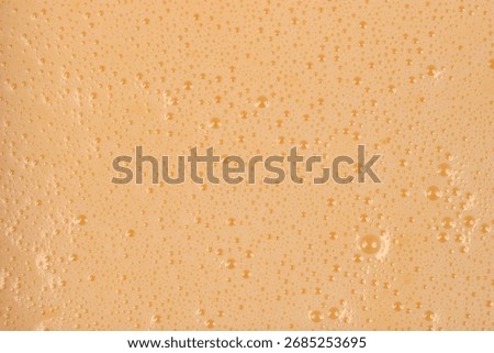 A full-frame, close-up shot captures the texture of a smooth, light beige liquid batter covered in tiny foam bubbles.