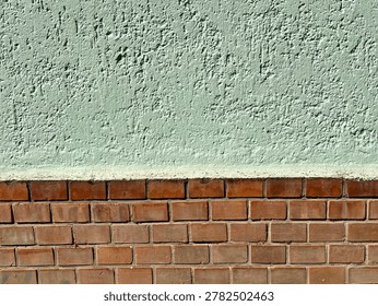 A full-frame, eye-level shot capturing a textured architectural background divided horizontally into two distinct sections. The top half features a rough, light pastel green stucco or plaster wall finish, while the bottom half consists of a rustic red brick wall with neat mortar joints, beautifully illuminated by bright, direct sunlight.