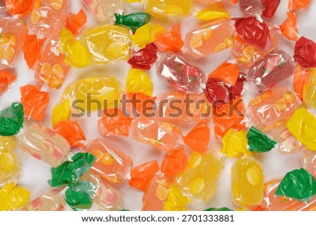A full-frame, vertical close-up of a dense scattering of various fruit-flavored jelly candies individually wrapped in brightly colored cellophane, covering a white background.