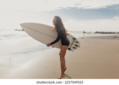 Full-lenght photo of exited lovely cute woman with loose wavy hair wearing black swimsuit having fun and enjoying vacation with surfboard on sandy beach with ocean view.  - Powered by Shutterstock