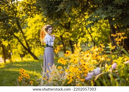 Full-lenght portrait of a young slender woman in a 1910s costume. Lady walking in the garden using an old-fashioned sun umbrella