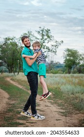 Full-length Authentic Family Portrait. Young Casual Dad With Son Hugging And Looking Into Camera. Father And Child Walking In Countryside. Daily Lives. Everyday Activities.