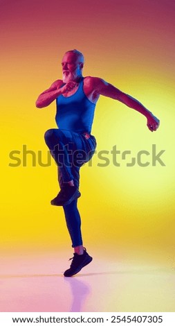 Full-length dynamic image of muscular elderly man in sportswear in motion, training against gradient yellow background in neon light. Concept of sport, active elderly lifestyle, health care