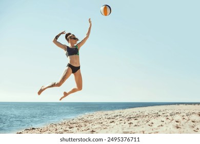 Full-length dynamic image of young woman in sunglasses and s swimwear playing beach volleyball, hitting ball in a jump. Blue sky and sea background. Concept of sport, summer, nature, active lifestyle - Powered by Shutterstock