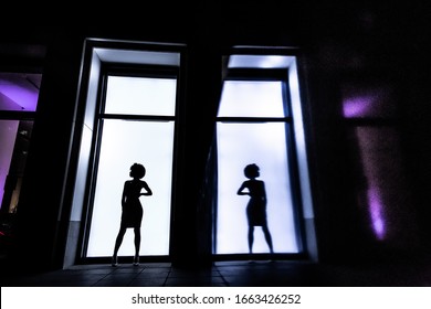 Full-length female silhouette on a rectangular window background. A woman stands and looks away. Her figure is reflected on the wall. Lifestyle