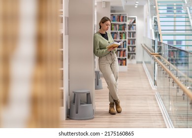 Full-length of focused mature woman bookworm in library. Pensive middle-aged woman bibliophile with book enjoying reading, gaining knowledge from books, learning new skills. Lifelong Learning