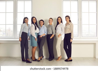 Full-length Group Portrait Of Happy Successful Stylish Young Women In Their 20s And 30s. Professional Team Of Company Workers Or Business Partners Standing Together In New Office And Smiling At Camera