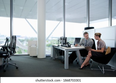 A full-length horizontal view of a businessman and businesswoman working together on a digital tablet at the desk in an office - Shutterstock ID 1868703301