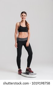 Full-length Image Of Female Sport Trainer Measuring Her Weight After Fitness Standing On Scale Isolated Over Gray Background