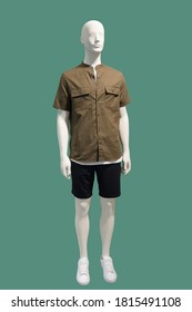 Full-length male mannequin dressed in brown short sleeve button-down shirt and black shorts, isolated on green background. No brand names or copyright objects.