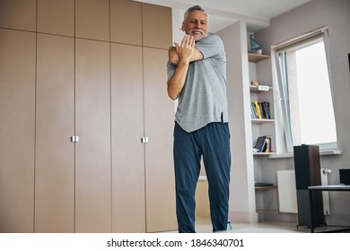 Full-length Photo Of An Elderly Man Stretching His Arms While Exercising At Home