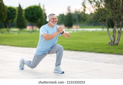 Full-length photo of happy smiling retired sportsman in sportswear and headphones doing front squat on one leg forward with hands folded outside in city park during routine workout in morning - Shutterstock ID 2131333253