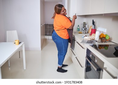 Full-length Photo Of Joyous African American Woman Standing In Kitchen With Bowl And Smiling At Laptop Screen