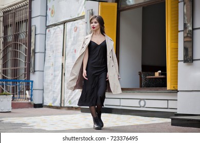 Full-length Photo Of Style Businesswoman Dressed In Black Dress Is Walking On The City With Charming Smile And Posing At Camera. Street Style, Fashion Look.