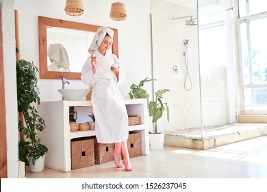 Full-length photo of woman in bathrobe with cream in her hands in bathroom. - Powered by Shutterstock