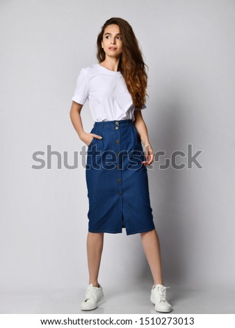 Full-length photo of a young brunette girl with long hair in a white blouse and blue skirt. on a light background.