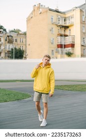 Full-length photo of a young man in stylish summer clothes, walking on the playground against the backdrop of the architecture of the old town, looking away. Vertical - Shutterstock ID 2235173263