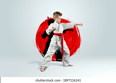 Full-length portrait of a boy in a white kimono with a red belt against the background of a red circle. Karate concept, training, goal, training, achievement