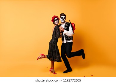 Full-length Portrait Of Funny Zombies Dancing In Studio. Indoor Photo Of Dead Couple Celebrating Halloween Together.