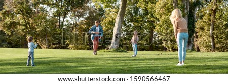 Full-length portrait of happy family of four playing with disc on a green meadow with grass. Family, kids and nature concept. Horizontal shot.
