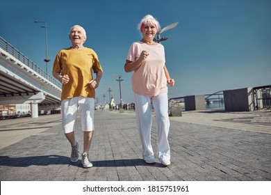 Full-length Portrait Of A High-spirited Senior Lady And Her Husband Power Walking Along The Quay