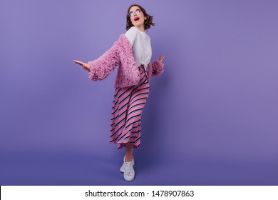 Full-length portrait of inspired young lady in fashionable clothes posing on purple background. Jocund european girl in sunglasses dancing with smile in studio.