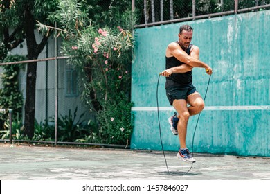 Full-length portrait of middle aged sportsman having training and doing rope jumping outdoors. Sport, fitness, street workout concept. Horizontal shot