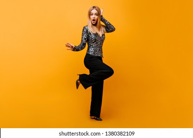 Full-length portrait of pleasant lady in stylish black pants. Photo of surprised glamorous woman isolated on yellow background.
