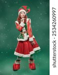 Full-length portrait of a pretty Christmas fairy elf girl in a beautiful bright costume on a green studio background. Tales for Christmas and New Year.