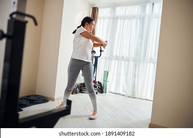 Full-length Portrait Of A Serious Well-built Dark-haired Caucasian Woman Performing A Standing Trunk Rotation Exercise