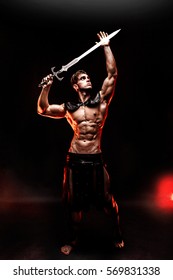 Full-length portrait of sexy young warrior holding sword and looking away while posing against fire. Copyspace