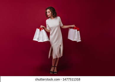 Full-length portrait of slim graceful lady holding bags from store. Indoor shot of fashionable white woman wears long dress.