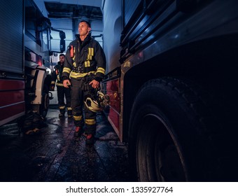 Full-length Portrait Of Two Brave Firemen In Protective Uniform Walking Between Two Fire Engines In The Garage Of The Fire Station