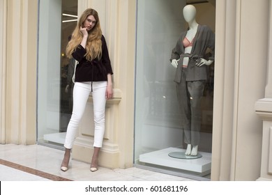 Full-length Portrait, Young Beautiful Blonde Woman In White Pants And Corduroy Jacket Stands In The Shop Window