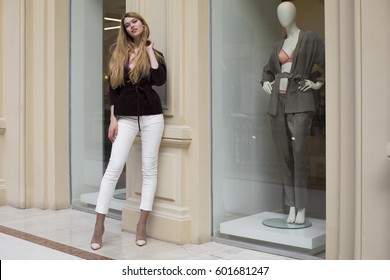 Full-length Portrait, Young Beautiful Blonde Woman In White Pants And Corduroy Jacket Stands In The Shop Window