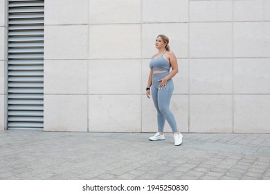 Full-length portrait of young fit plus size woman in grey sports bra and leggings standing outdoors - Powered by Shutterstock