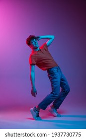 Full-length portrait of young man in casual clothes dancing isolated on gradient pink-purple background in neon light. Concept of human emotions, facial expression, youth culture. Copy space for ad.