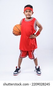 Full-length profile studio shot of an Asian boy in a red jersey holding a basketball