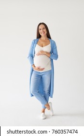Full-length shot of a joyful pregnant woman with hands on belly posing at camera 
