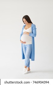 Full-length shot of loving pregnant woman looking at belly while posing in studio 
