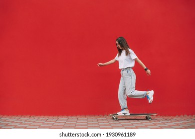 Full-length shot of a skater woman wearing fancy clothes and riding her skateboard in front of a red wall with a copy space on a city street.
