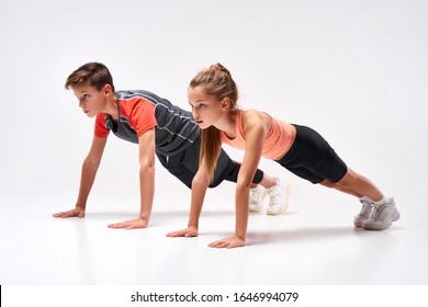 Full-length shot of teenage boy and girl engaged in sport, looking away while doing push-ups. Isolated on white background. Training, active lifestyle, team concept. Horizontal shot - Powered by Shutterstock