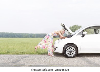 Full-length side view of woman examining broken down car on country road - Powered by Shutterstock