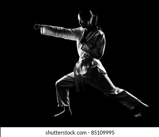 full-length silhouette portrait of beautiful martial arts girl in kimono exercising karate kata on black